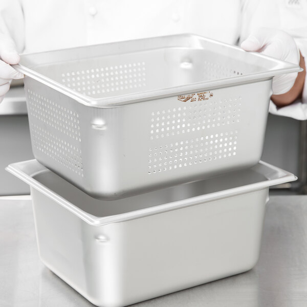 A person holding a large Vollrath stainless steel pan with holes in the bottom.