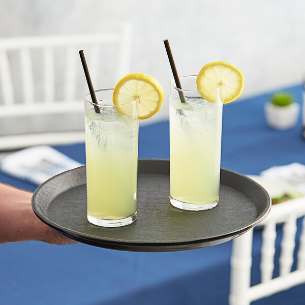 A black round non-skid serving tray holding two glasses of lemonade with lemon slices and straws.