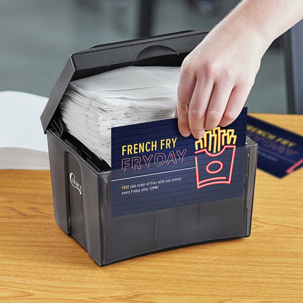 A black tabletop napkin dispenser filled with napkins and a promotional card on the front.