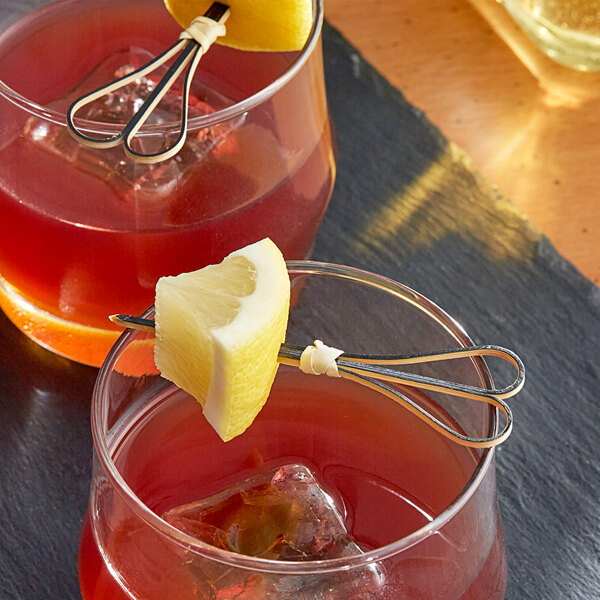 A black bamboo heart-shaped food pick skewering a lemon wedge, placed on the rim of a cocktail glass.