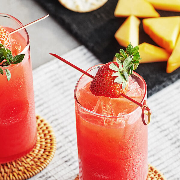 A red bamboo knot food pick skewering a strawberry garnish in a glass of red beverage.