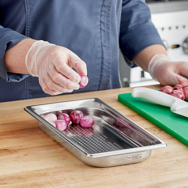 A woman using a knife to cut onions on a cutting board in a stainless steel steam table pan.