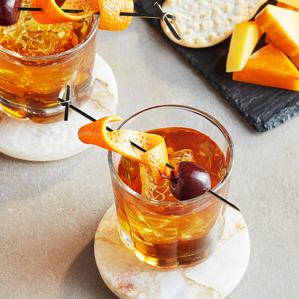 A black bamboo knot food pick skewering an orange peel and cherry, placed in a cocktail glass.
