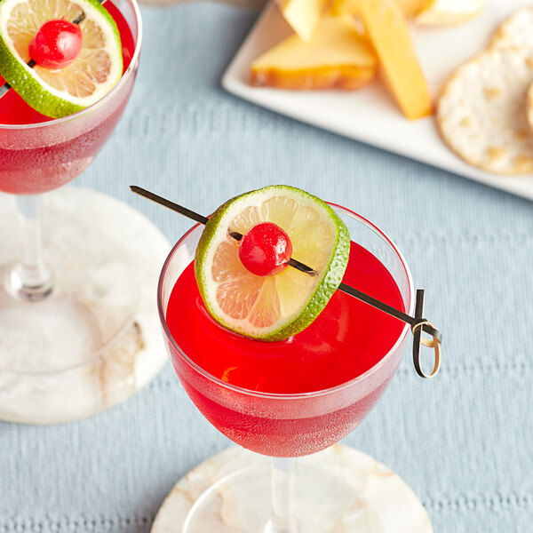 A black bamboo knot food pick skewering a lime slice and cherry, garnishing a red cocktail.