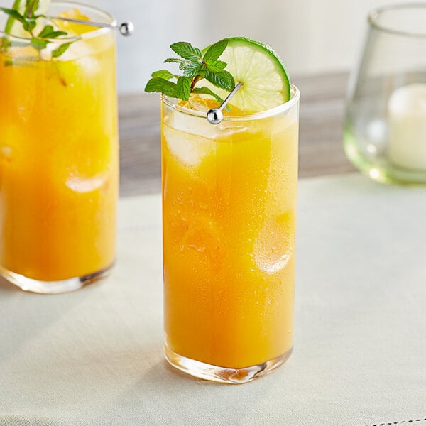 A tall glass of orange-yellow passion fruit drink with ice, garnished with a lime slice and mint sprig.