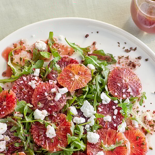 A salad featuring arugula, blood orange slices, and crumbled cheese on a white plate.