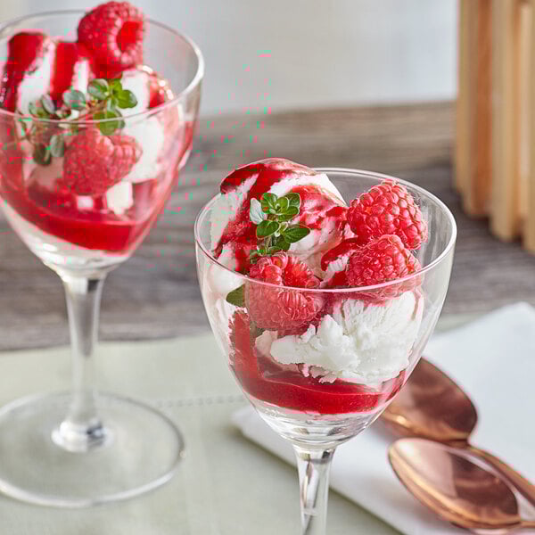 A glass dessert dish filled with vanilla ice cream, fresh raspberries, raspberry puree, and a sprig of mint.