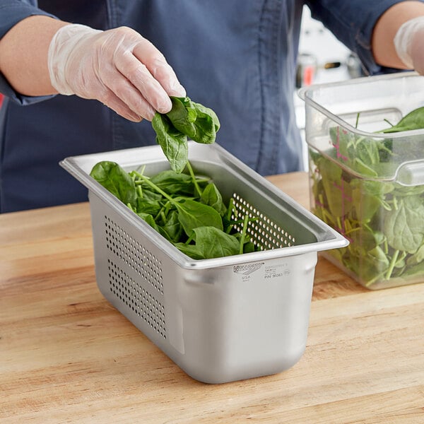 A person using a Vollrath stainless steel hotel pan to hold spinach leaves.