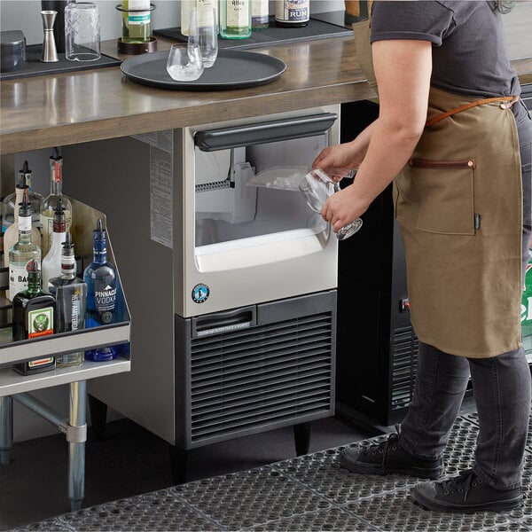 A commercial undercounter ice machine with a built-in storage bin being used in a bar setting.