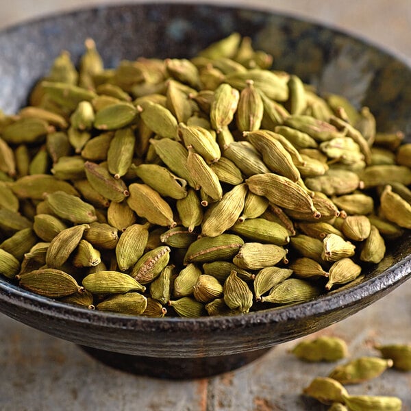 A bowl filled with whole green cardamom pods.