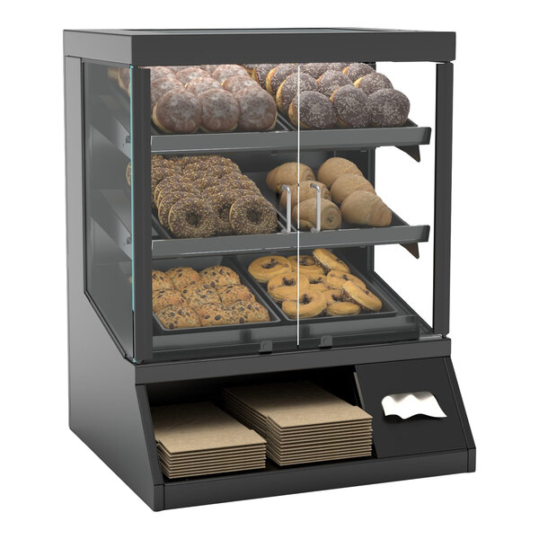 A self-service countertop bakery display case with three shelves of assorted baked goods and compartments for napkins and paper bags.