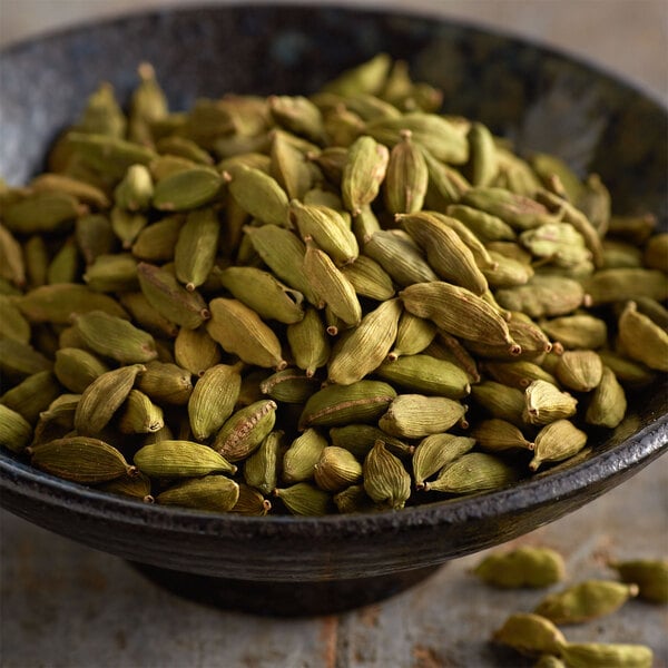 A bowl filled with whole green cardamom pods.