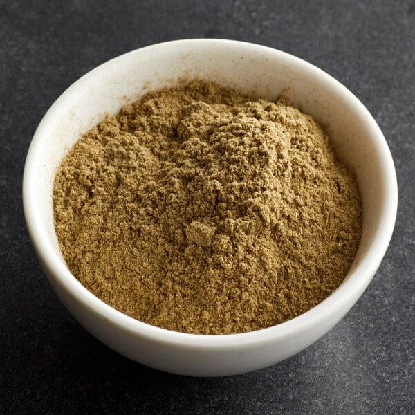 A white bowl filled with a light brown, finely ground powder on a dark surface.