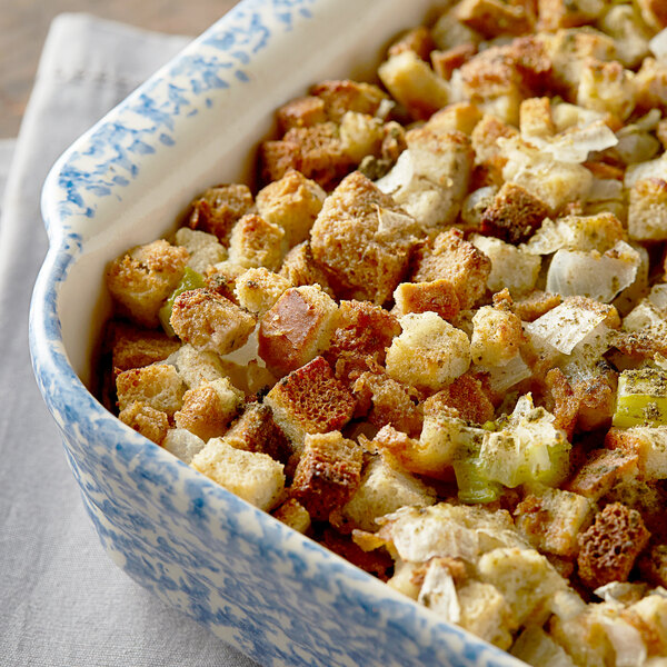 A casserole dish filled with baked bread stuffing containing cubes of bread, celery, onions, and herbs.