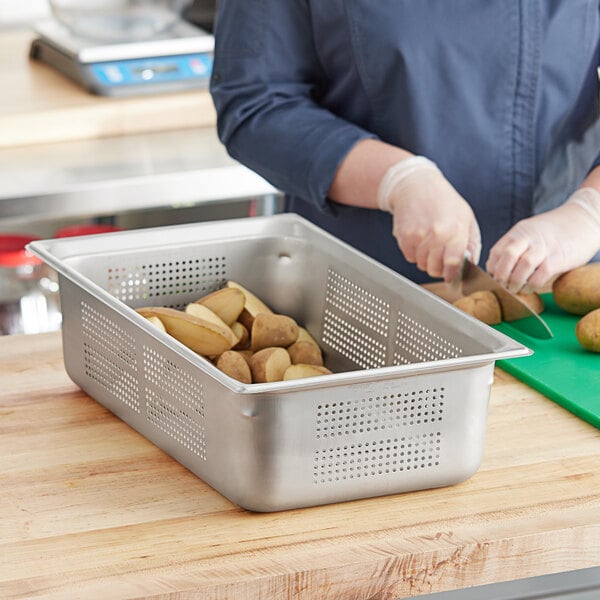 A woman using a knife to cut potatoes in a Vollrath stainless steel steam table pan.