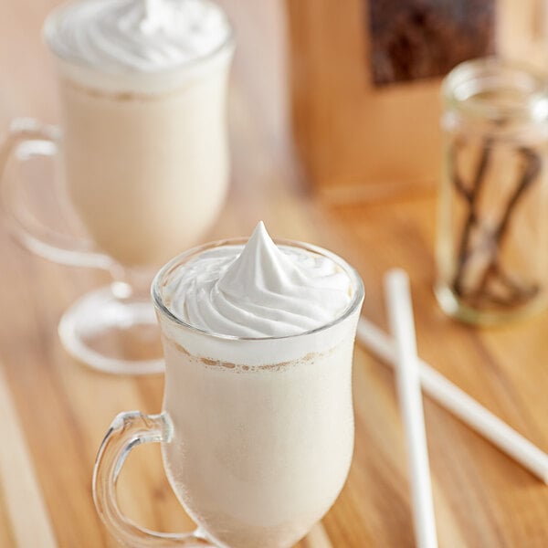 A glass mug filled with a vanilla blended ice coffee topped with whipped cream.