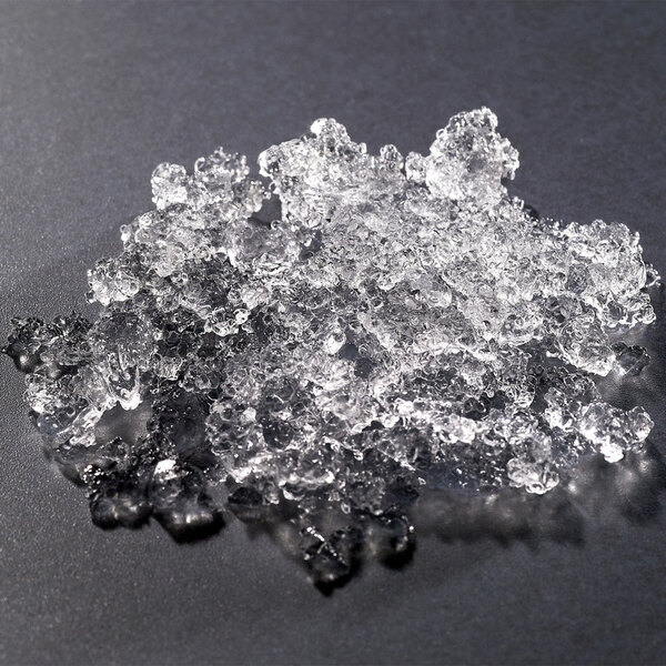 A pile of clear, irregularly shaped flake ice pieces on a dark surface.