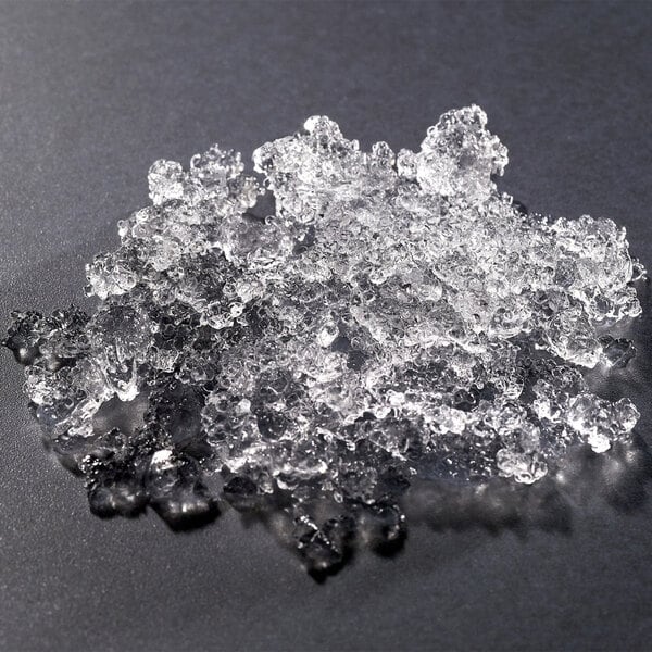 A pile of clear, irregularly shaped cubelet ice pieces on a dark surface.