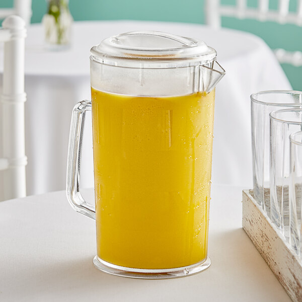 A clear plastic pitcher with a lid, filled with orange juice.