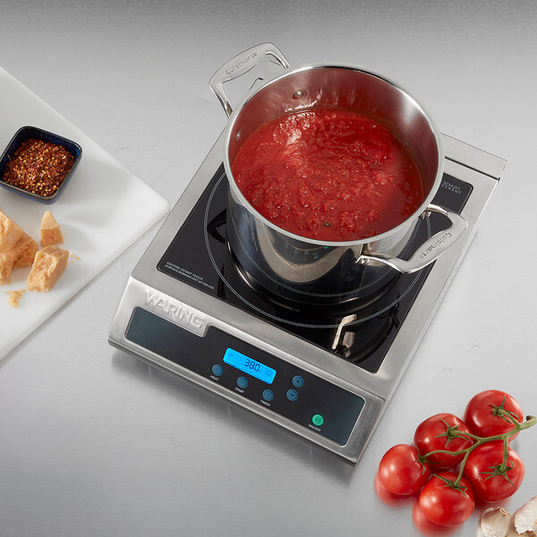 A Waring WIH400X 13-inch electric induction range with a pot of tomato sauce on top, shown on a stainless steel surface.