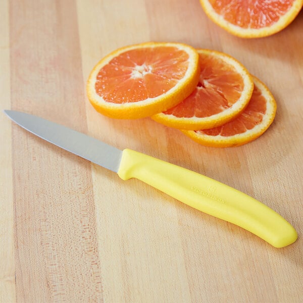 A Victorinox paring knife with a yellow handle next to slices of oranges.