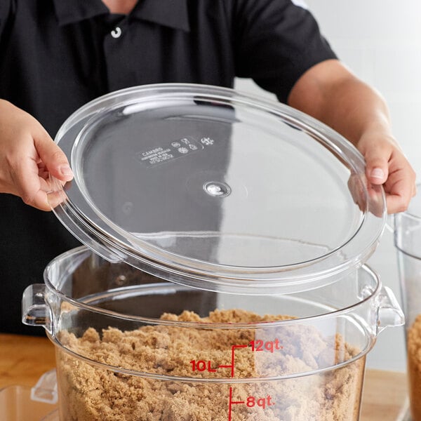 A clear round polycarbonate food storage container lid being placed on a large container filled with brown sugar.