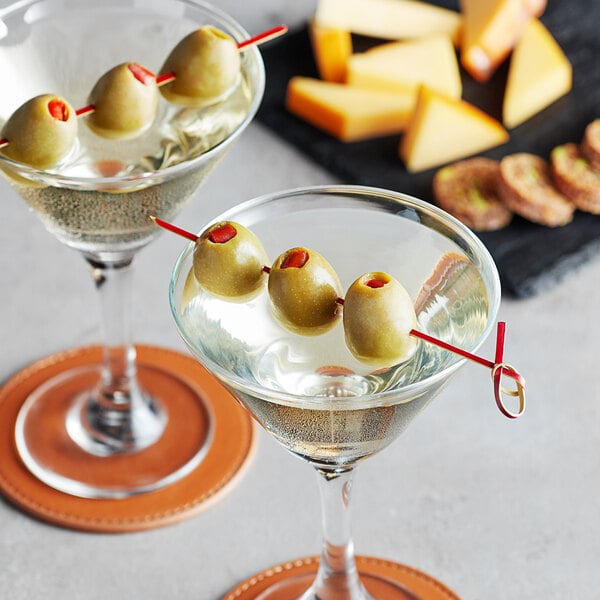 A red bamboo knot food pick skewering three green olives, placed in a martini glass.