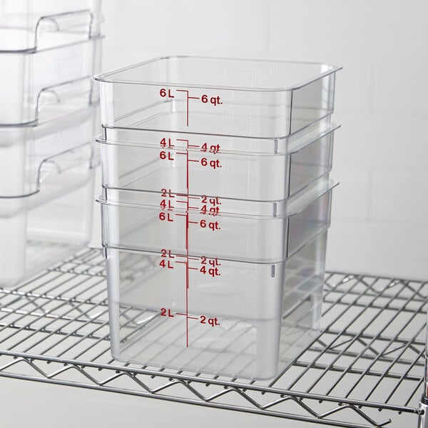 A stack of clear square polycarbonate food storage containers with red measurement markings, each with a 6-quart capacity.
