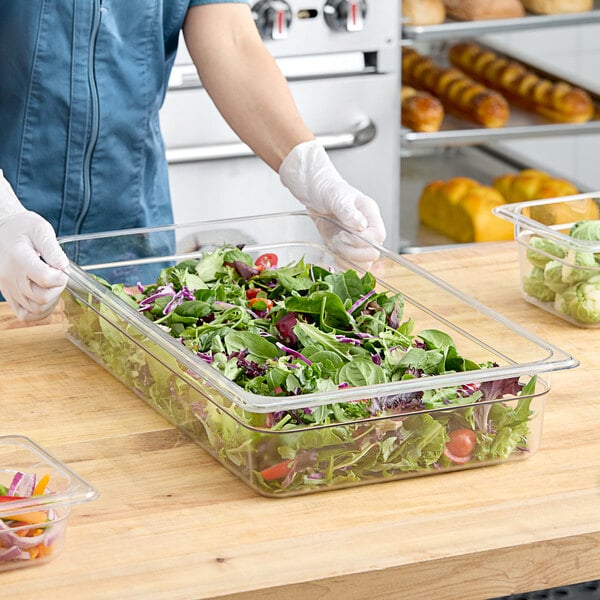 A clear polycarbonate full-size food pan filled with mixed salad greens and vegetables.