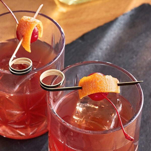 A black bamboo loop food pick skewering an orange peel and cherry, placed on a cocktail glass.