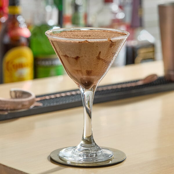 A clear martini glass filled with a chocolate cocktail, placed on a bar counter.