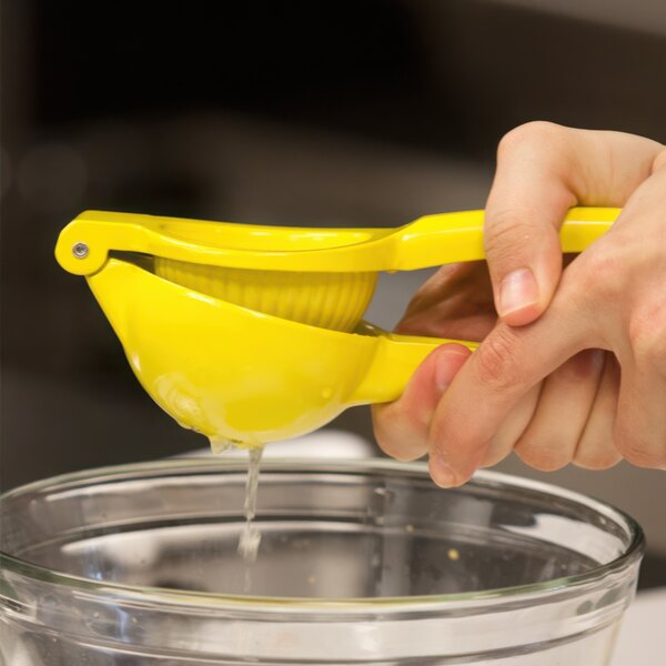 A person squeezing lemon juice into a yellow bowl.
