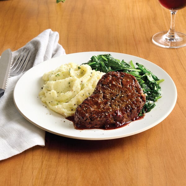 A plate with a plant-based vegan steak filet, mashed potatoes, and sautéed greens.