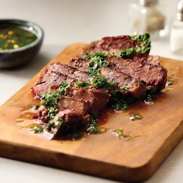A sliced plant-based vegan steak filet topped with green herb sauce on a wooden cutting board.