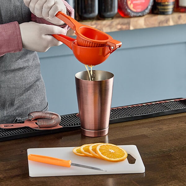 Sliced oranges being poured into a copper cup on a Choice white bar size cutting board.