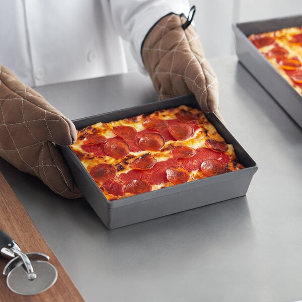 A rectangular hard coat anodized aluminum Detroit-style pizza pan containing a pepperoni pizza.