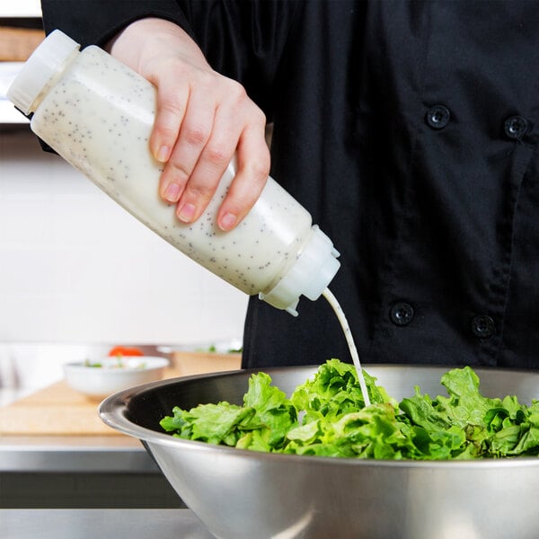 A person pouring dressing from a FIFO Innovations 16 oz. squeeze bottle with a thick dispensing valve onto a bowl of lettuce.