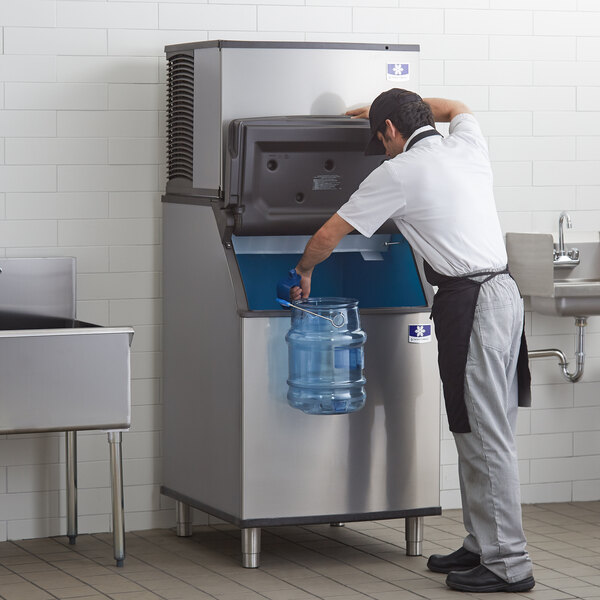 A commercial ice machine with a storage bin being used to fill a large water jug.