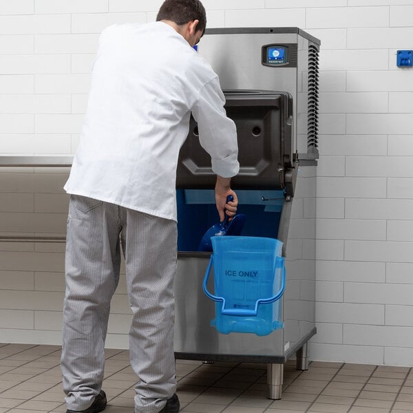 A commercial ice machine with a storage bin being used by a person in a professional kitchen setting.