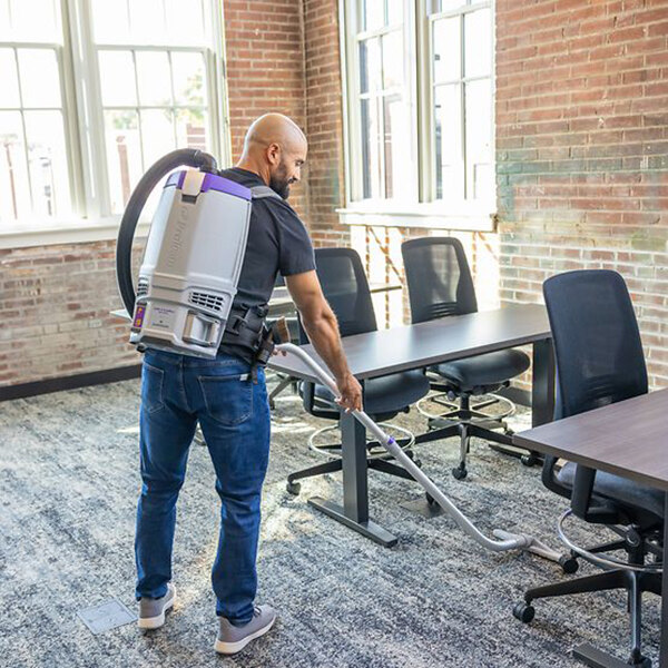 A cordless backpack vacuum being used to clean an office carpet.
