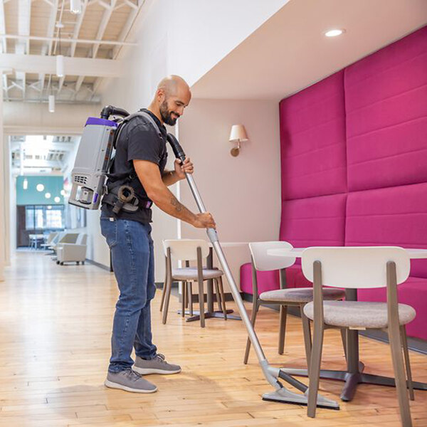 A cordless backpack vacuum being used to clean a hardwood floor in a modern indoor setting.