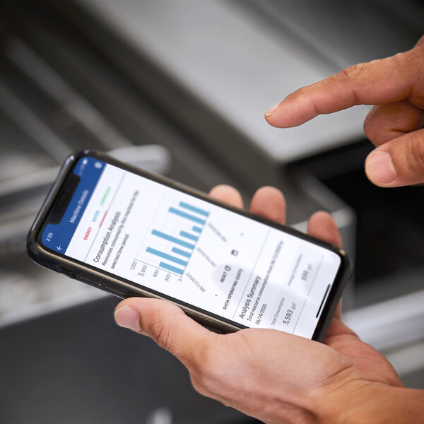 A person holding a smartphone displaying a bar graph and data analysis, likely related to the operation or monitoring of a commercial dishwasher.