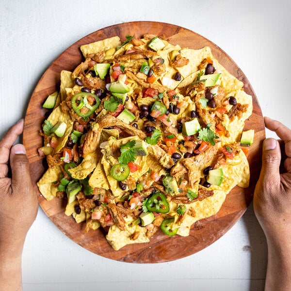 A plate of nachos topped with plant-based vegan wood-smoked shredded chicken, black beans, avocado, jalapeños, and fresh salsa.