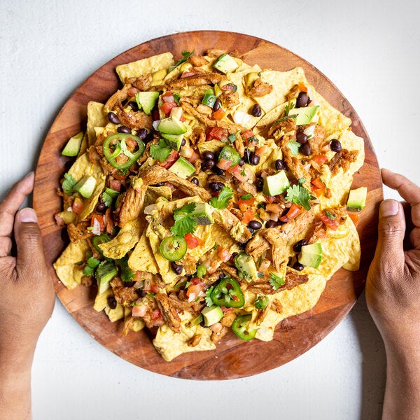 A plate of nachos topped with Barvecue plant-based vegan wood-smoked carnitas, black beans, avocado, jalapeños, and fresh salsa.
