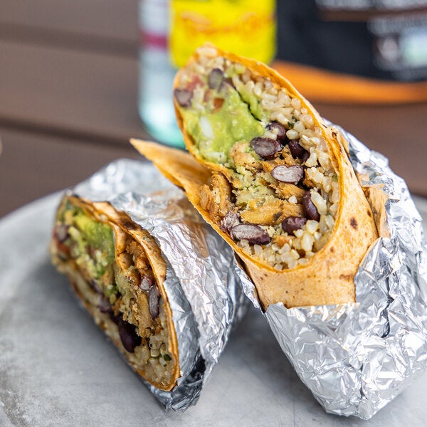 A foil-wrapped burrito cut in half, filled with plant-based vegan wood-smoked carnitas, rice, beans, and guacamole.