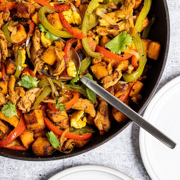 A skillet filled with plant-based vegan wood-smoked carnitas, sweet potatoes, bell peppers, onions, and cilantro.