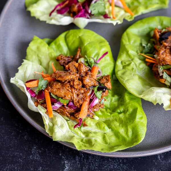 A plate of plant-based vegan wood-smoked barbecue pulled pork served in lettuce wraps with shredded vegetables.