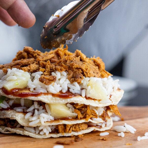 A stack of tortillas filled with plant-based vegan wood-smoked barbecue pulled pork, rice, pineapple, and sauce.