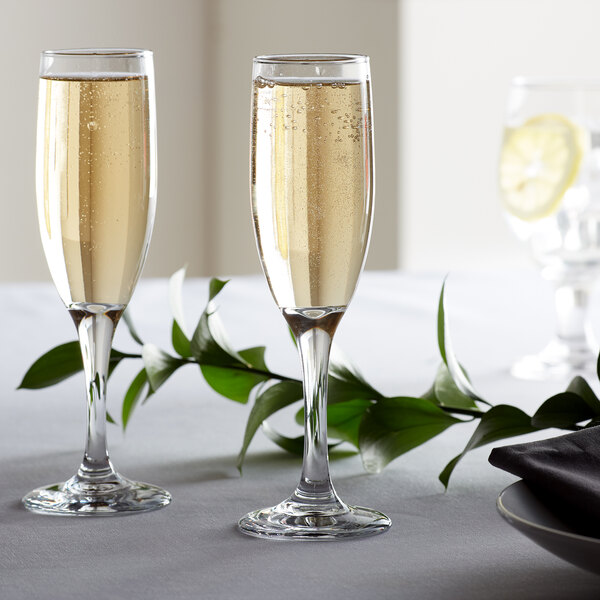 Two glasses of champagne on a table with a stem of leaves in the background