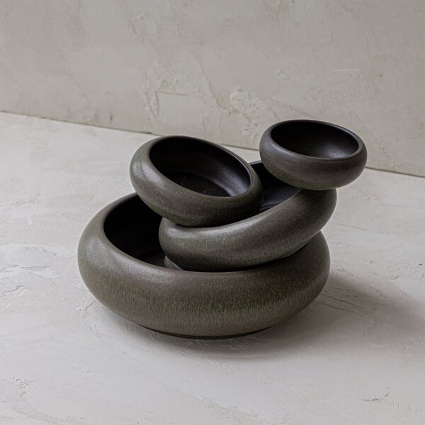 Four round, greenish-brown stoneware bowls are stacked inside each other on a light textured surface.